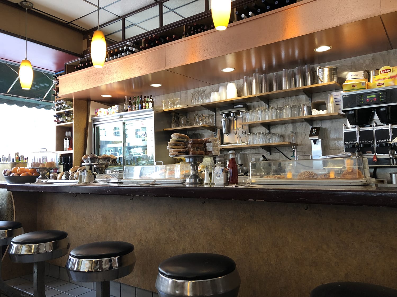 Cozy diner interior with bar stools, countertop, and a variety of pastries and drinks on display.