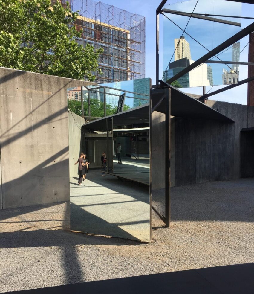 Child running through a mirrored outdoor art installation reflecting buildings and trees under a clear sky.