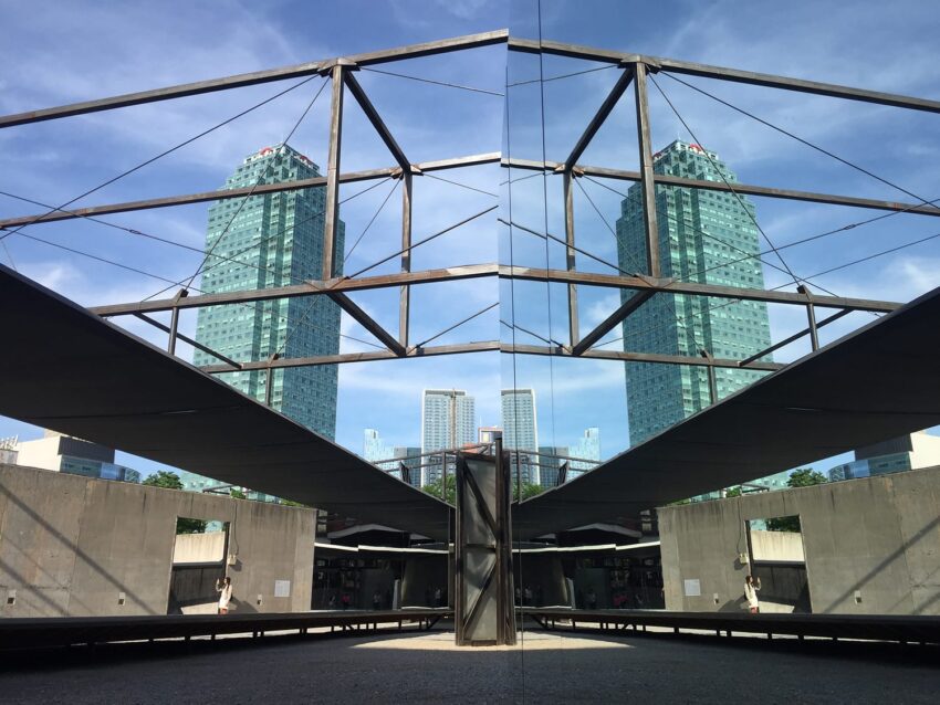 Art installation with geometric structures and skyscrapers in the background under a clear blue sky.