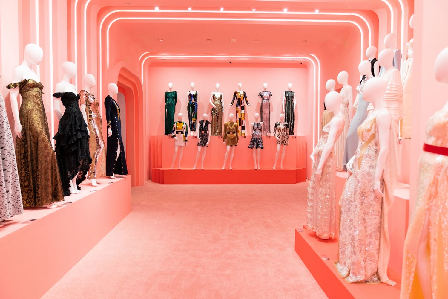 Fashion display with mannequins wearing elegant dresses in a pink-lit showroom with a modern, curved design.