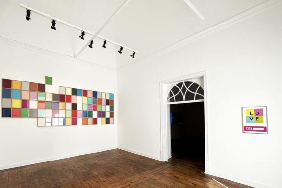 Art gallery interior with a colorful geometric wall display and a framed "LOVE" poster next to an arched doorway.