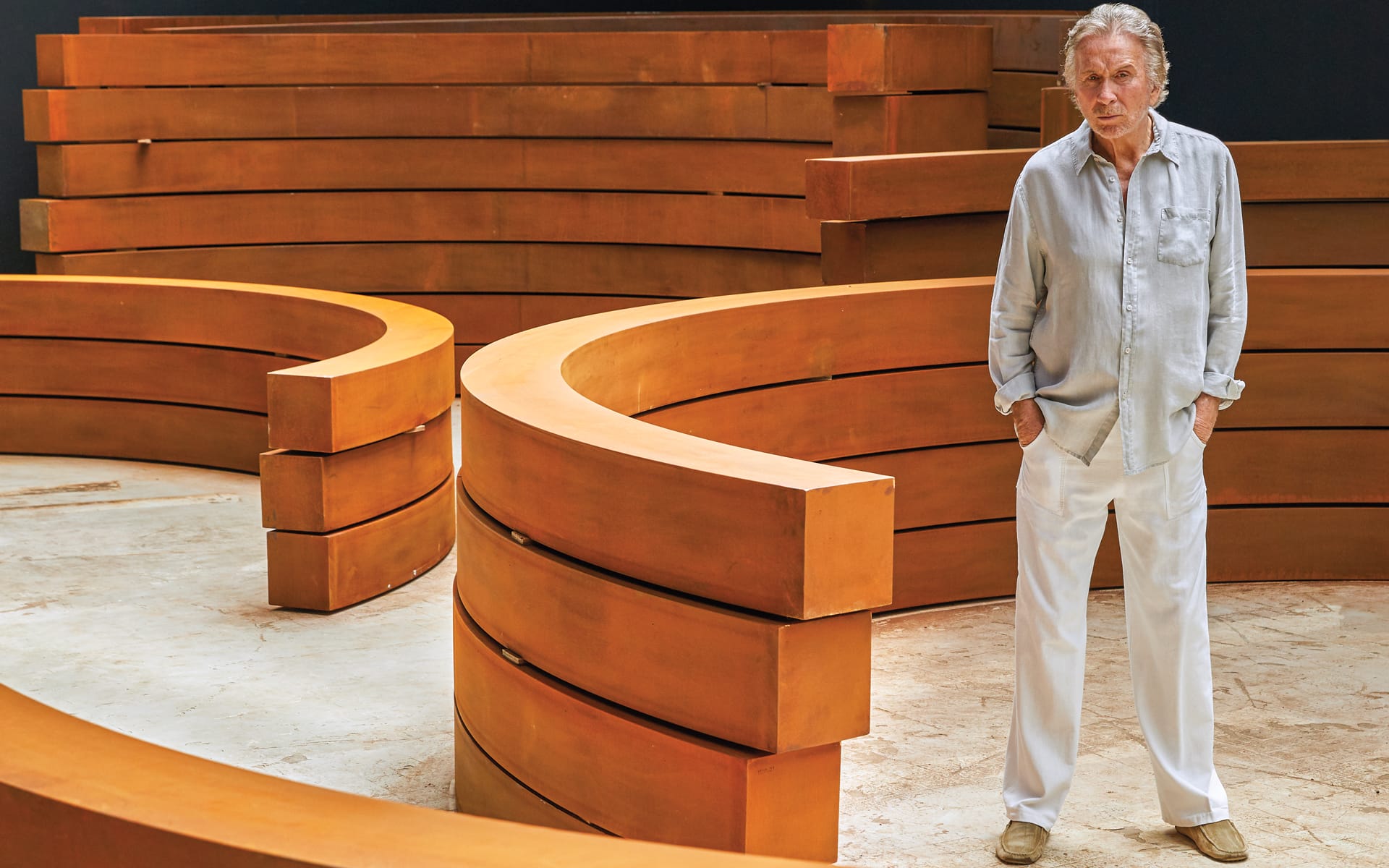 Man standing among large curved metal sculptures in a spacious gallery setting.