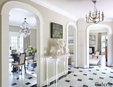 Elegant home interior with arched doorways, chandeliers, black and white floor tiles, and a dining area with large windows.