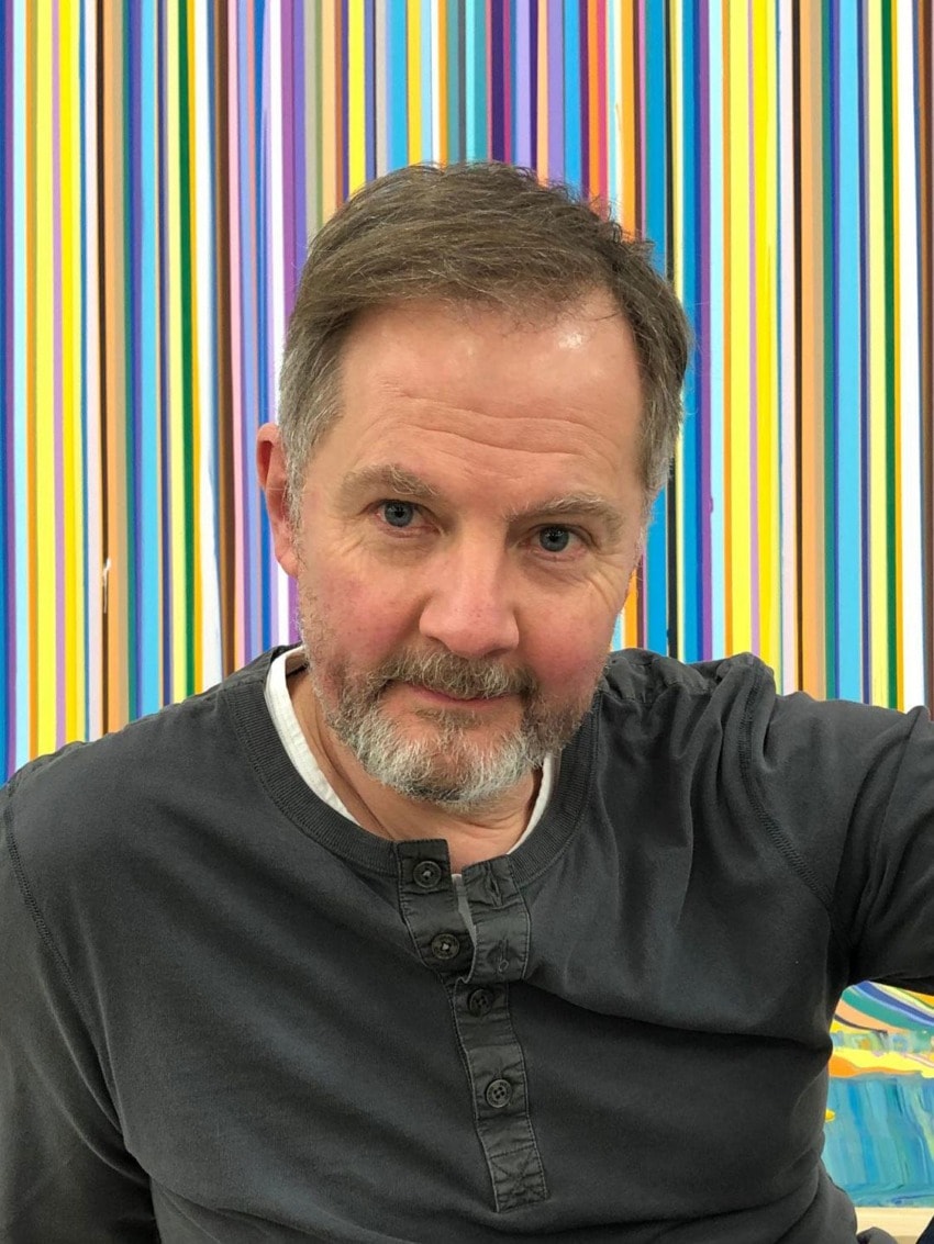 Smiling man in a gray shirt in front of a colorful striped background