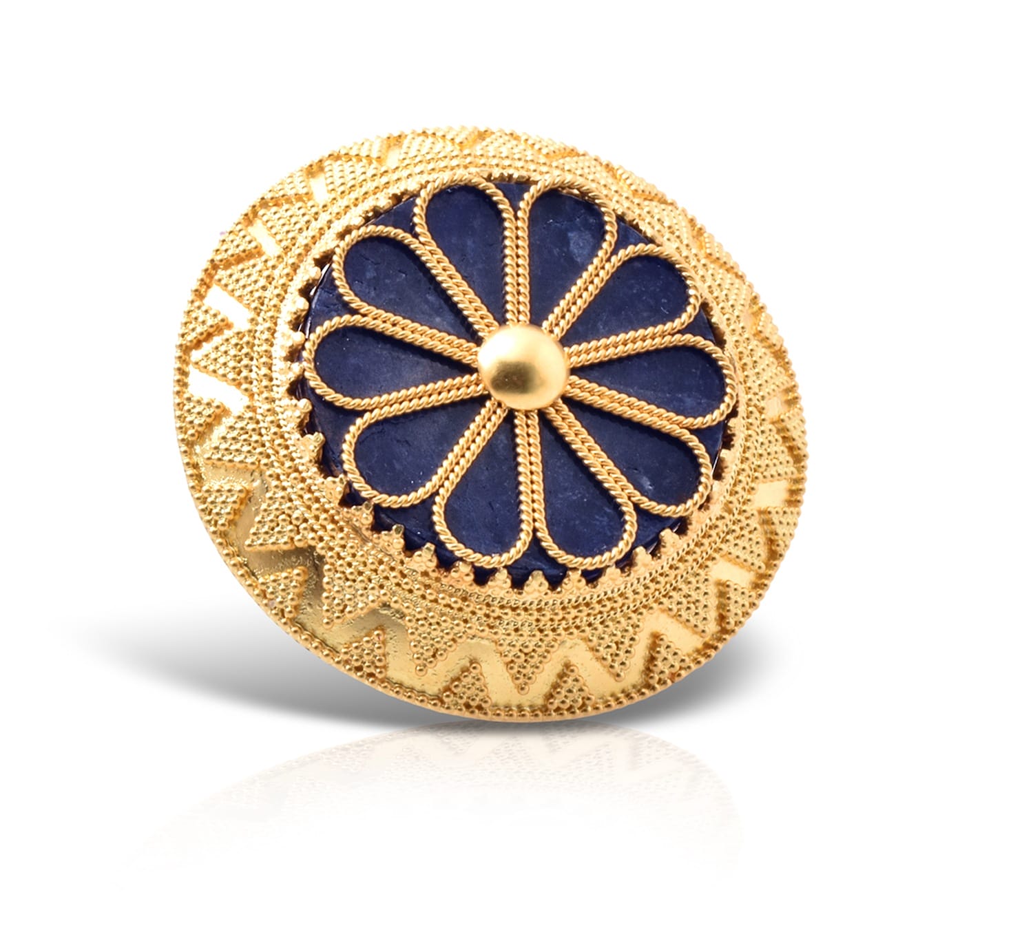 Round gold brooch with intricate blue floral design and zigzag patterns, casting a subtle reflection on white background.