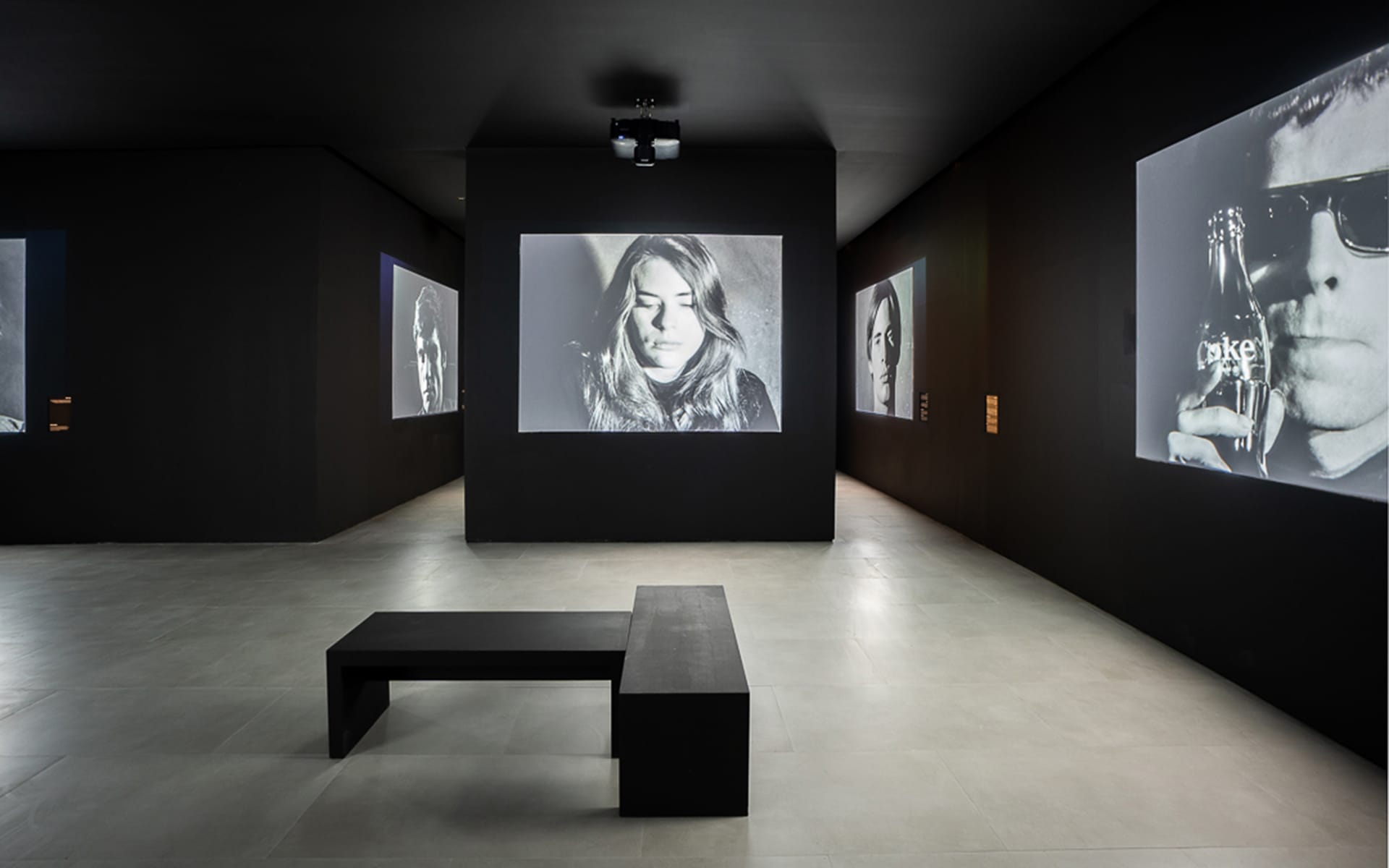 Art gallery featuring black and white portraits displayed on dark walls, with a bench in the center.