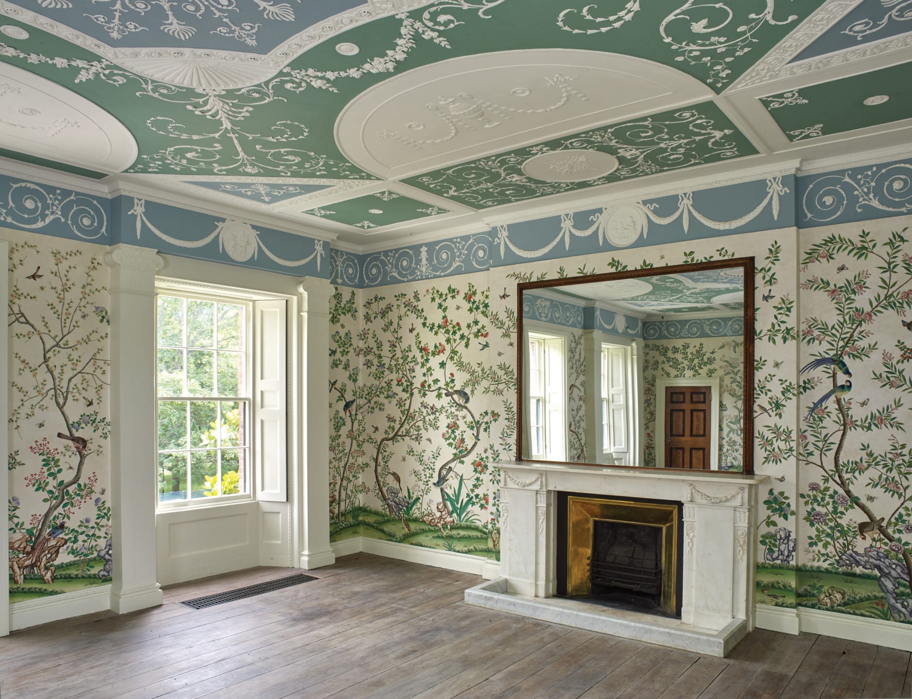 Ornate room with colorful floral wallpaper, wooden floor, large mirror above a fireplace, and detailed ceiling moldings.