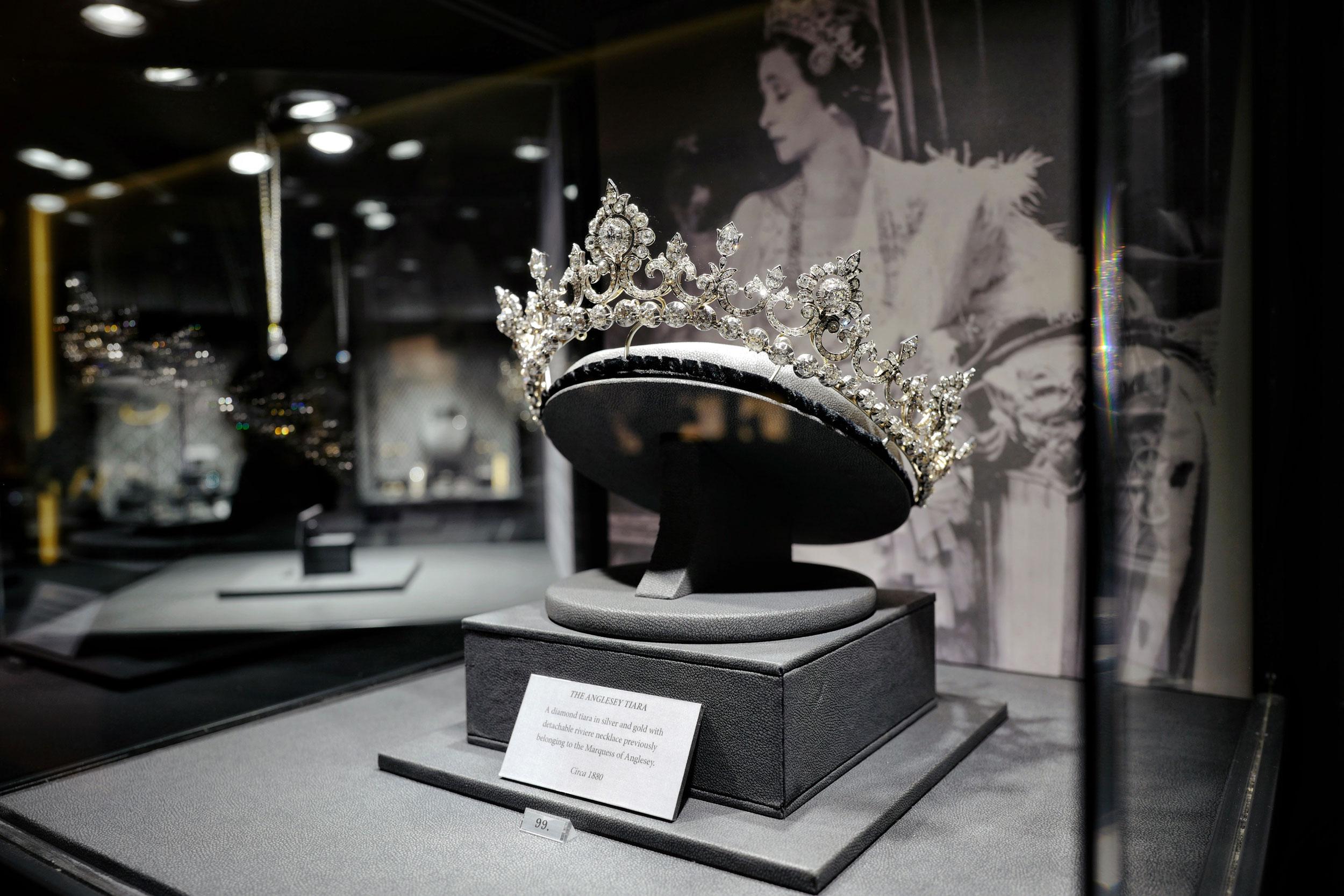 Elegant diamond tiara displayed in a glass case at a museum exhibition with a portrait in the background.