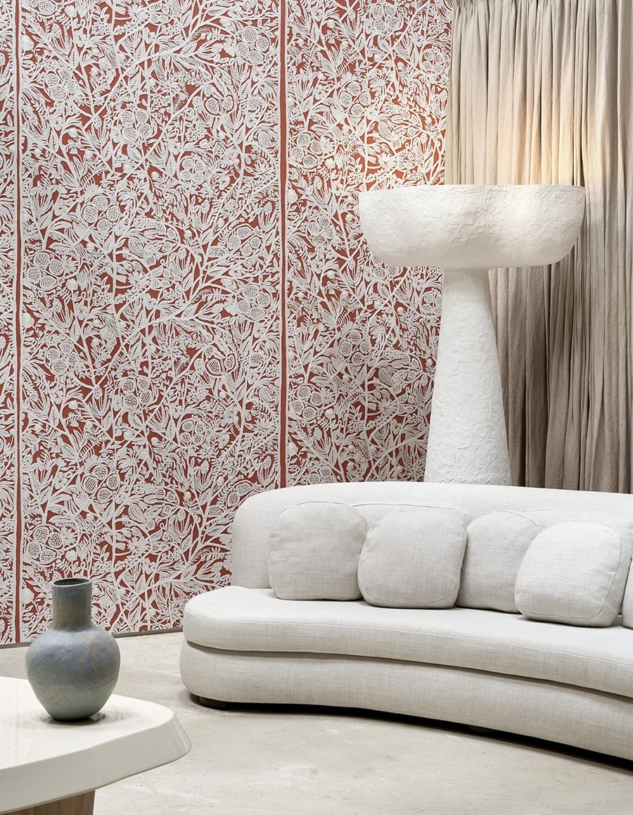 Modern living room with white curved sofa, tall textured lamp, decorative vase, and intricate red and white wall pattern.