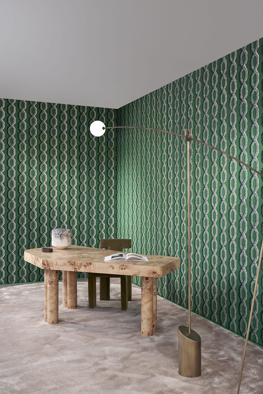Modern office with a wooden desk, green patterned wallpaper, a decorative vase, an open book, and a tall curved floor lamp.