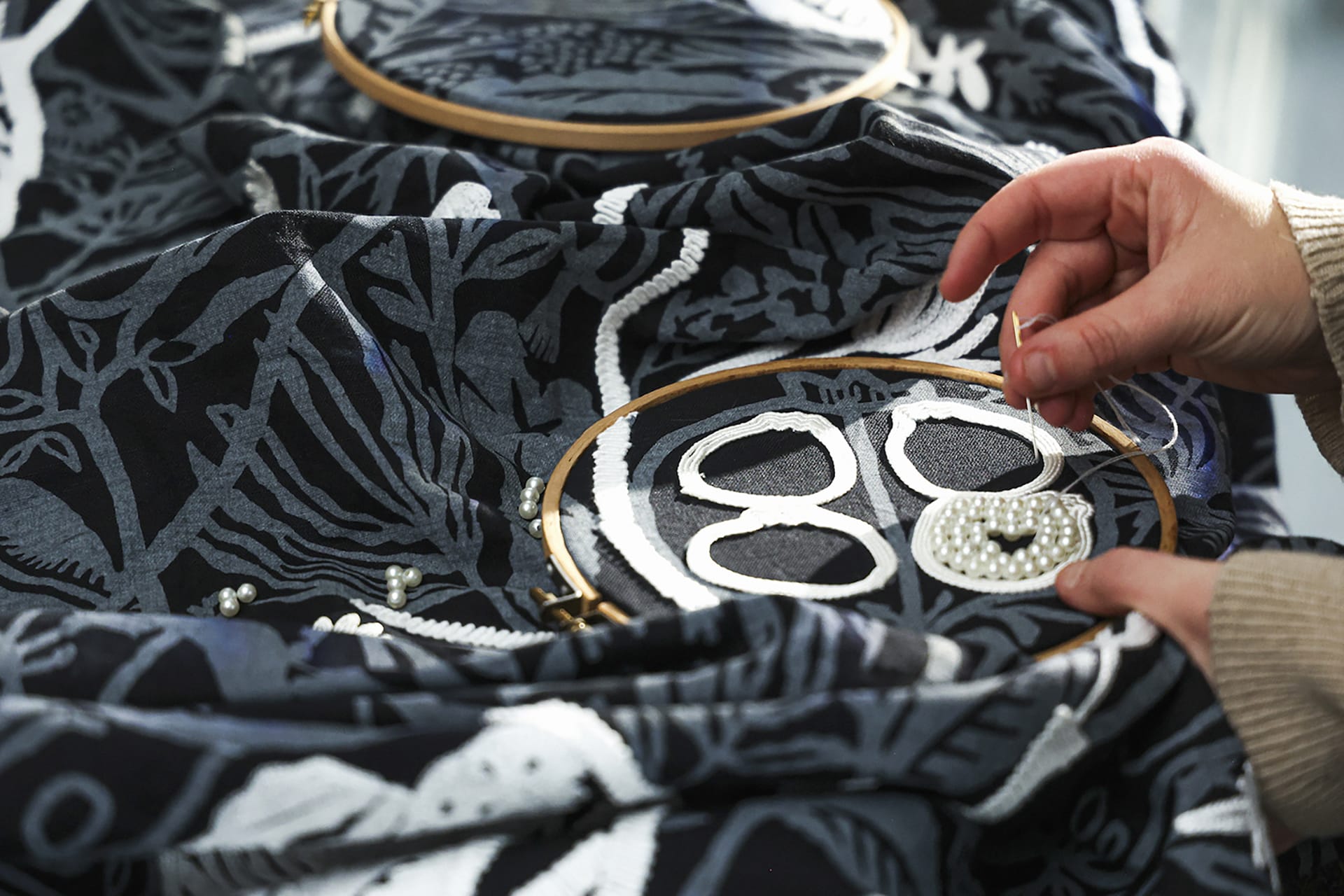 Hands embroidering a textile with intricate blue and white designs using a wooden embroidery hoop.