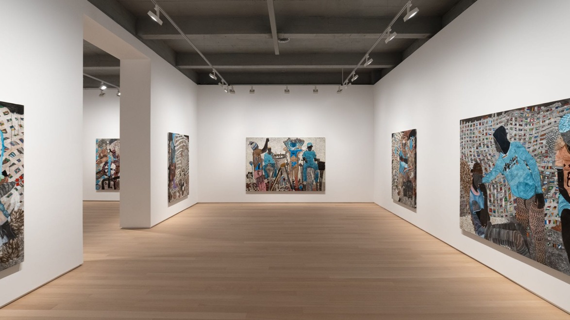 Art gallery interior with modern paintings on white walls, wooden floor, and overhead lighting.