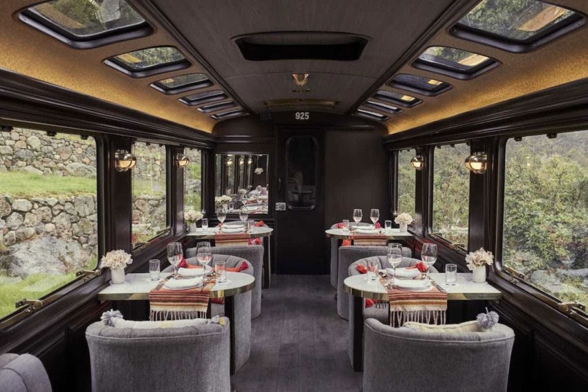 Luxurious train dining car with elegant table settings, scenic window views, and cozy gray seating.