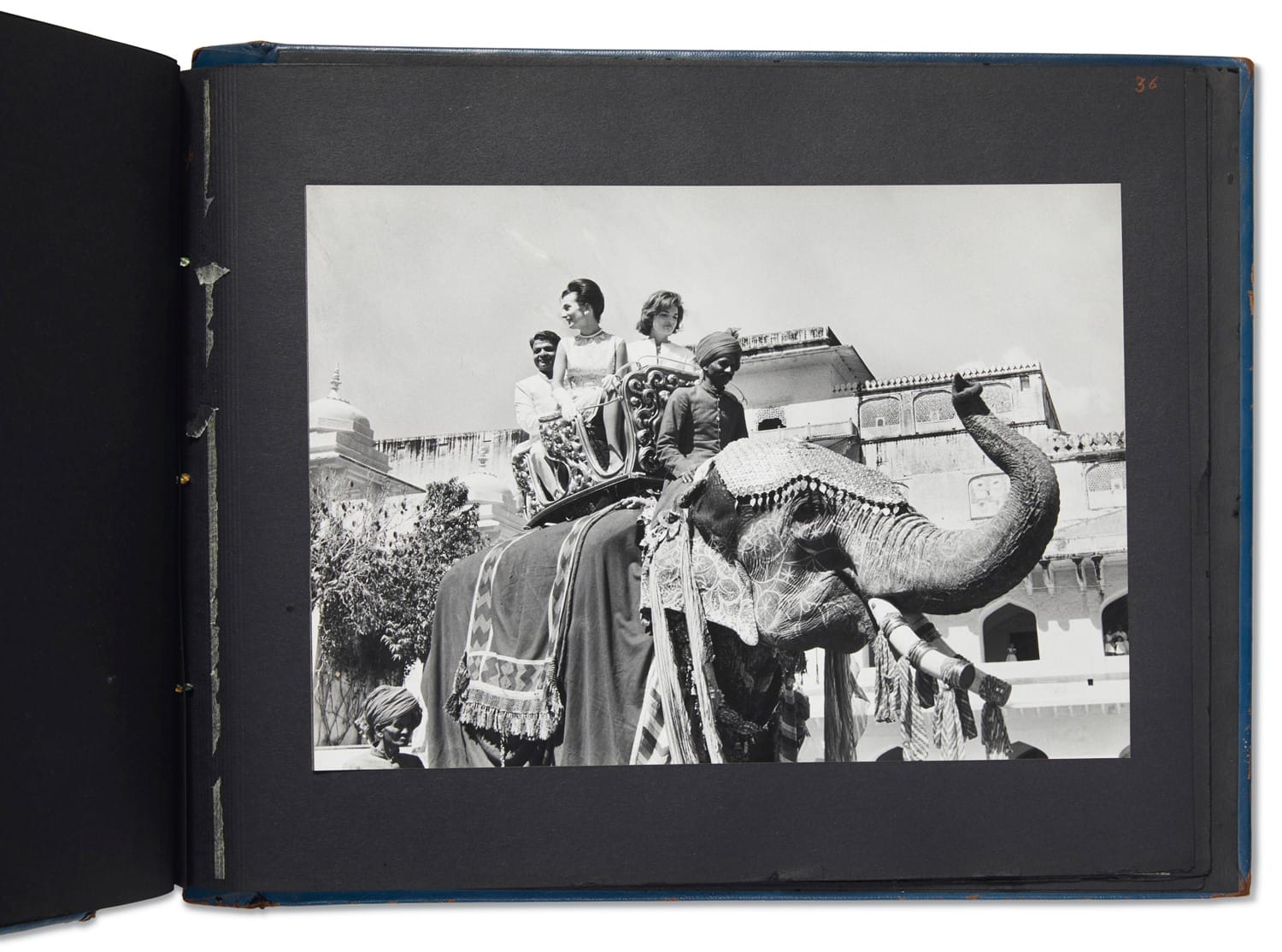 People riding a decorated elephant in a historic setting, wearing traditional attire; black and white photograph.