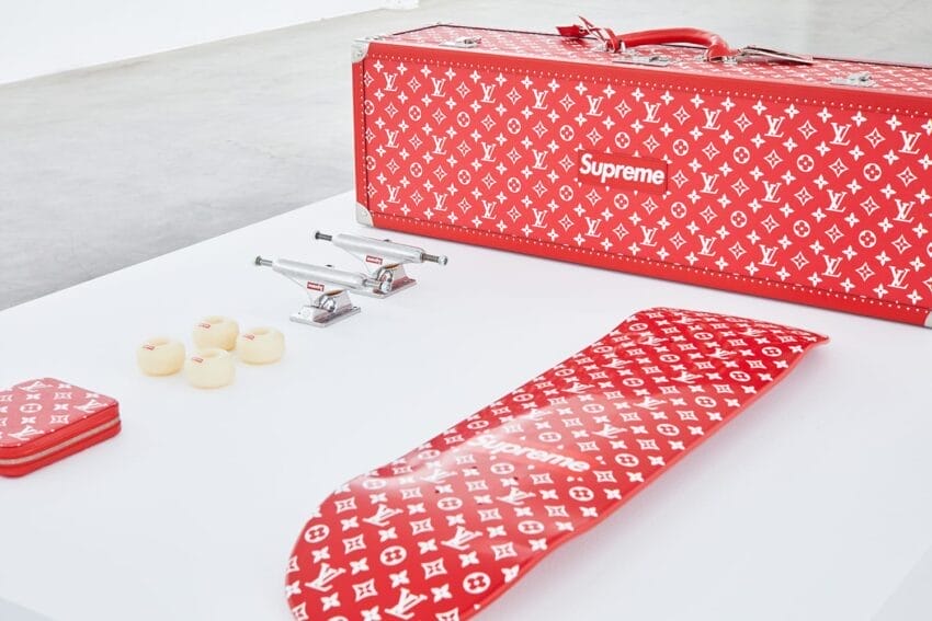 Red and white Supreme and Louis Vuitton branded skateboard set with case, deck, wheels, and trucks on a white surface.