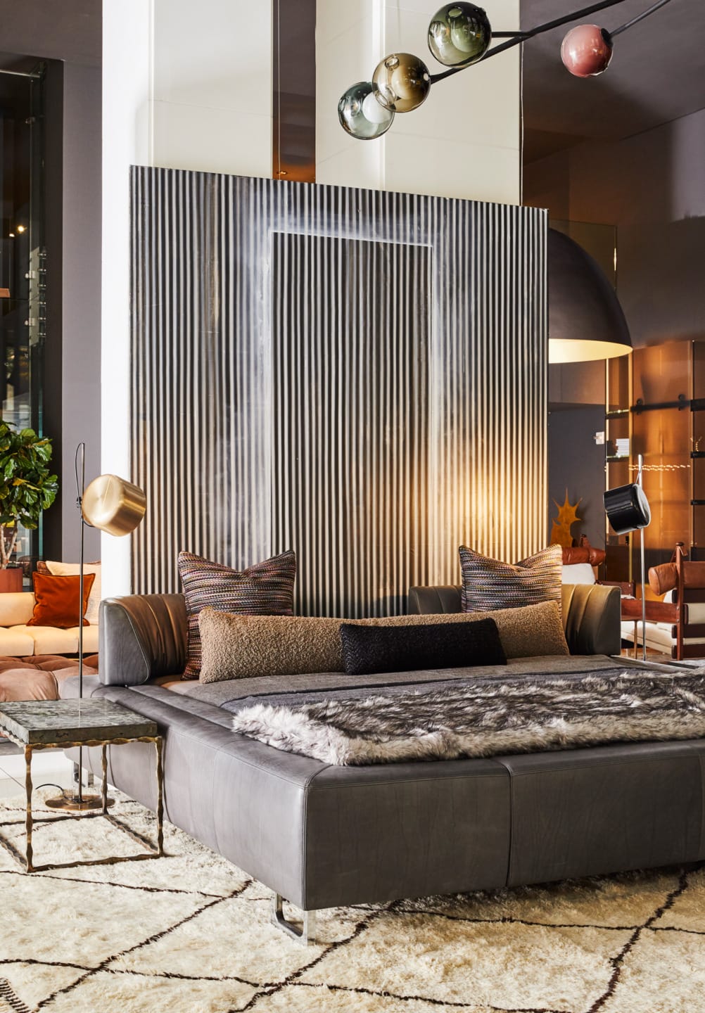 Modern living room with a large gray sofa, textured wall panel, stylish lamps, and geometric-patterned rug.