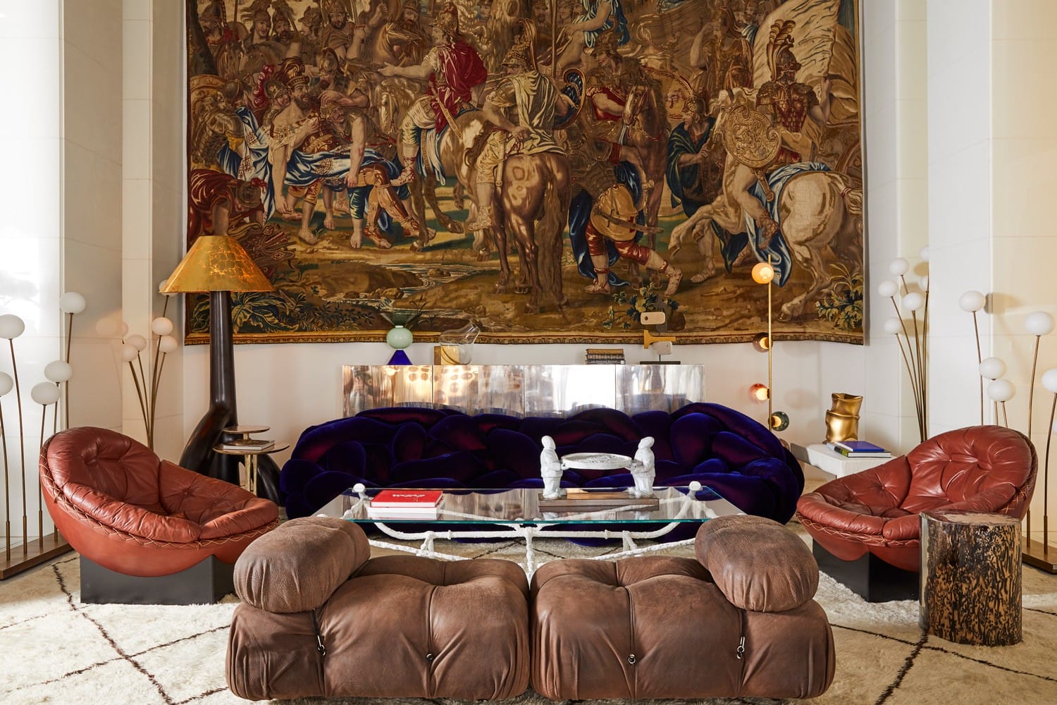 Vintage-style living room with a large tapestry, eclectic furniture, and various lamps on a patterned rug.