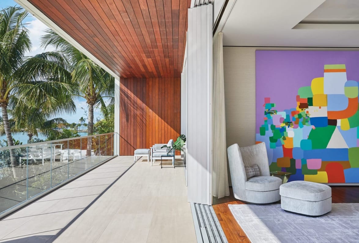 Modern balcony with large colorful abstract painting, wooden ceiling, cozy chairs, and tropical palm tree view.