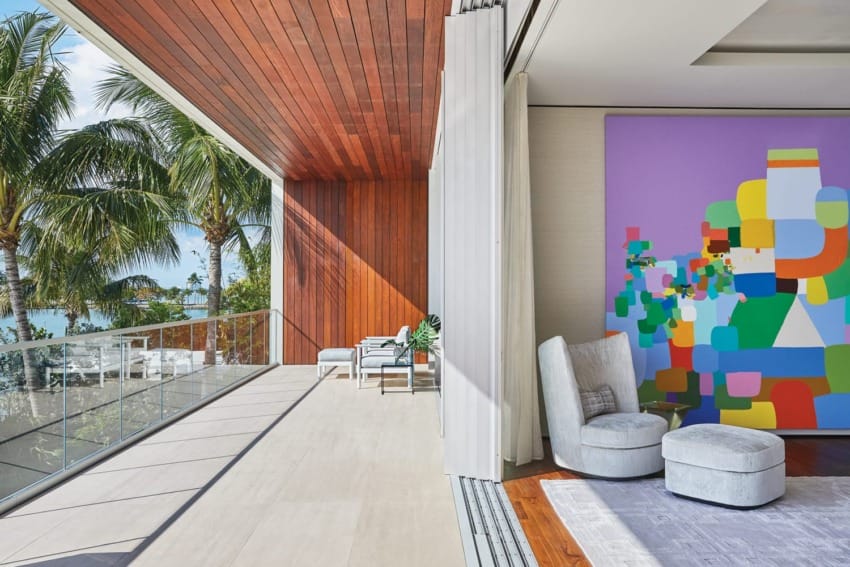 Modern balcony with large colorful abstract painting, wooden ceiling, cozy chairs, and tropical palm tree view.