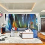 Modern living room with colorful abstract wall art, sleek furniture, geometric chandelier, and large windows.