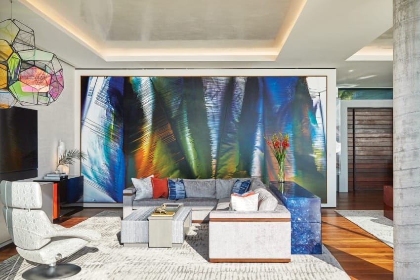 Modern living room with colorful abstract wall art, sleek furniture, geometric chandelier, and large windows.