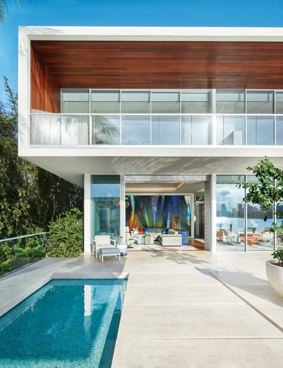 Modern two-story home with glass facade, pool, and outdoor seating area under a clear blue sky.