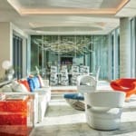 Modern living room with colorful furniture, large windows, abstract art, and a stylish dining area in the background.