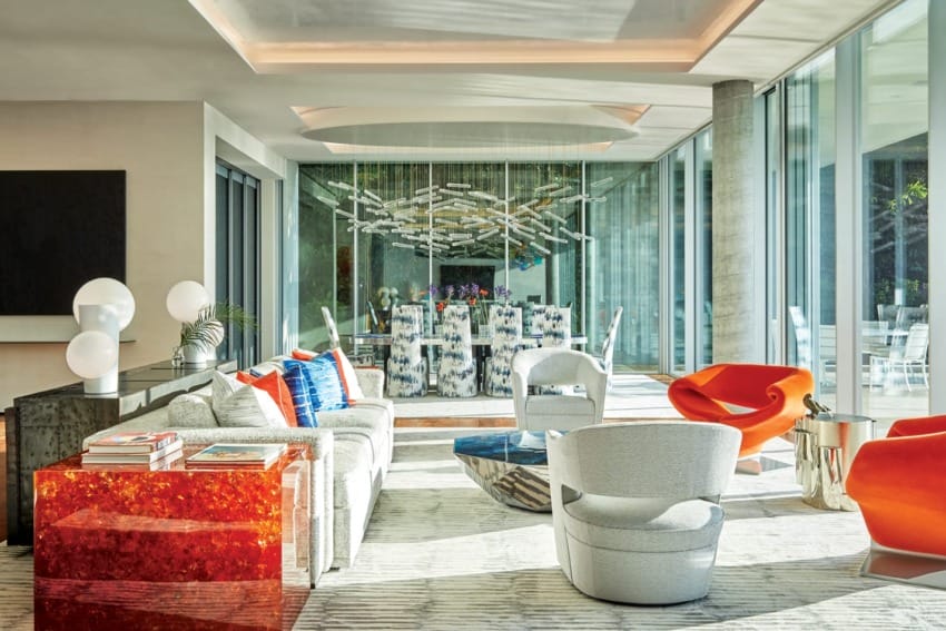 Modern living room with colorful furniture, large windows, abstract art, and a stylish dining area in the background.