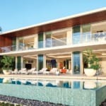 Modern luxury house with large glass windows, pool in foreground, surrounded by lush greenery and palm trees, under clear sky.