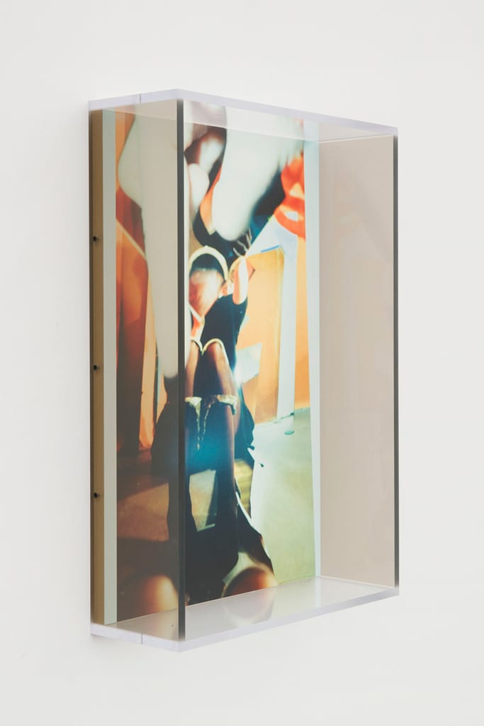 Artwork featuring abstract figures with vibrant colors in a clear shadow box frame, displayed against a plain wall.