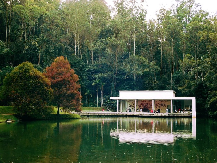 Modern white building surrounded by trees reflected in a peaceful lake.