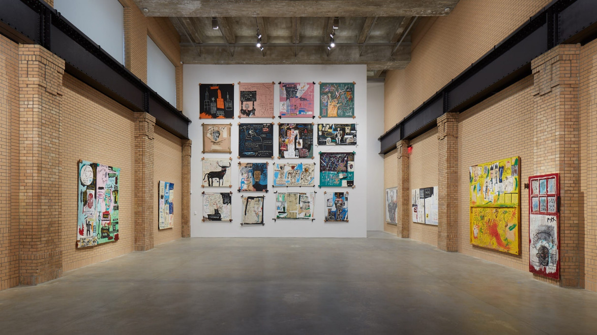 Art gallery with contemporary mixed media paintings displayed on brick walls and floor with a neutral tone.