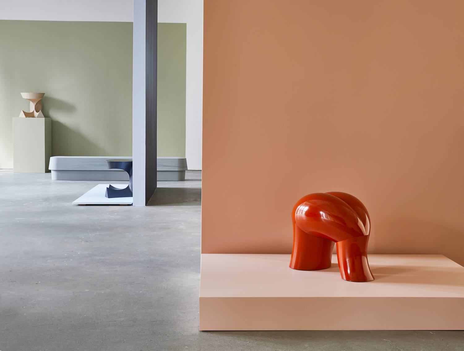 Colorful modern sculptures displayed in a minimalist gallery setting with pastel-colored walls and concrete floors.