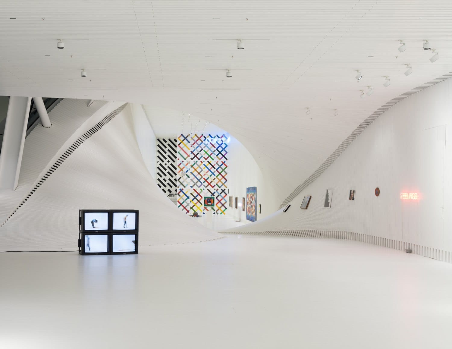 Modern art gallery with curved white walls, colorful wall art, and a TV display on a minimalist floor.