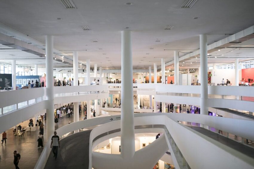 Modern art gallery interior with spiral ramps and large white columns, filled with visitors exploring exhibitions.