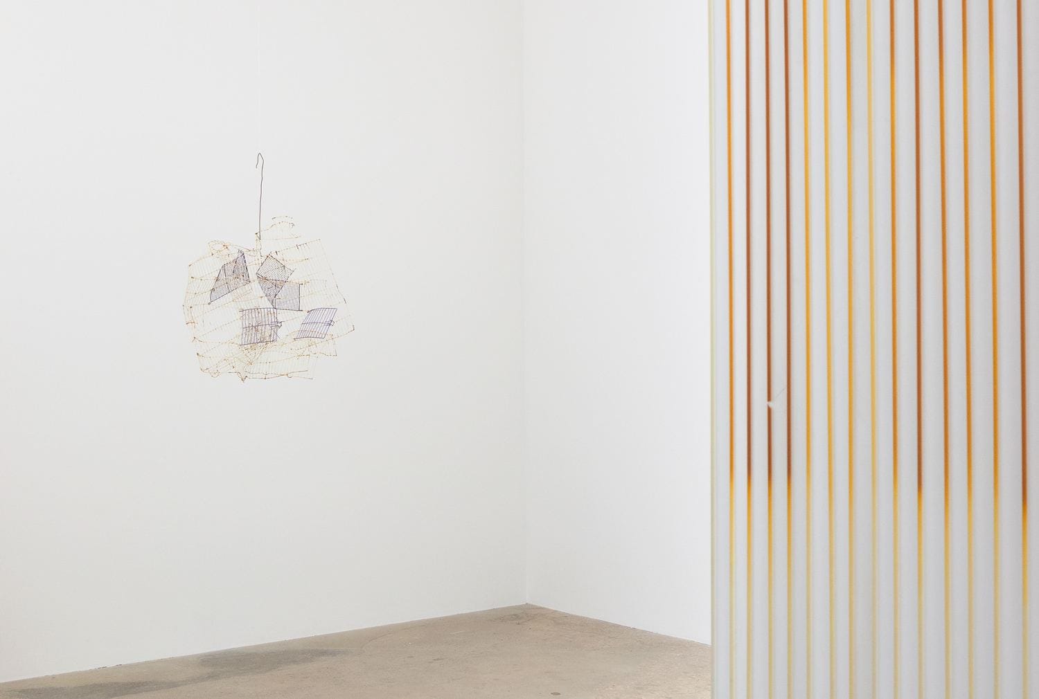 Minimalist art installation with abstract wall sculpture and striped divider in a white gallery space.