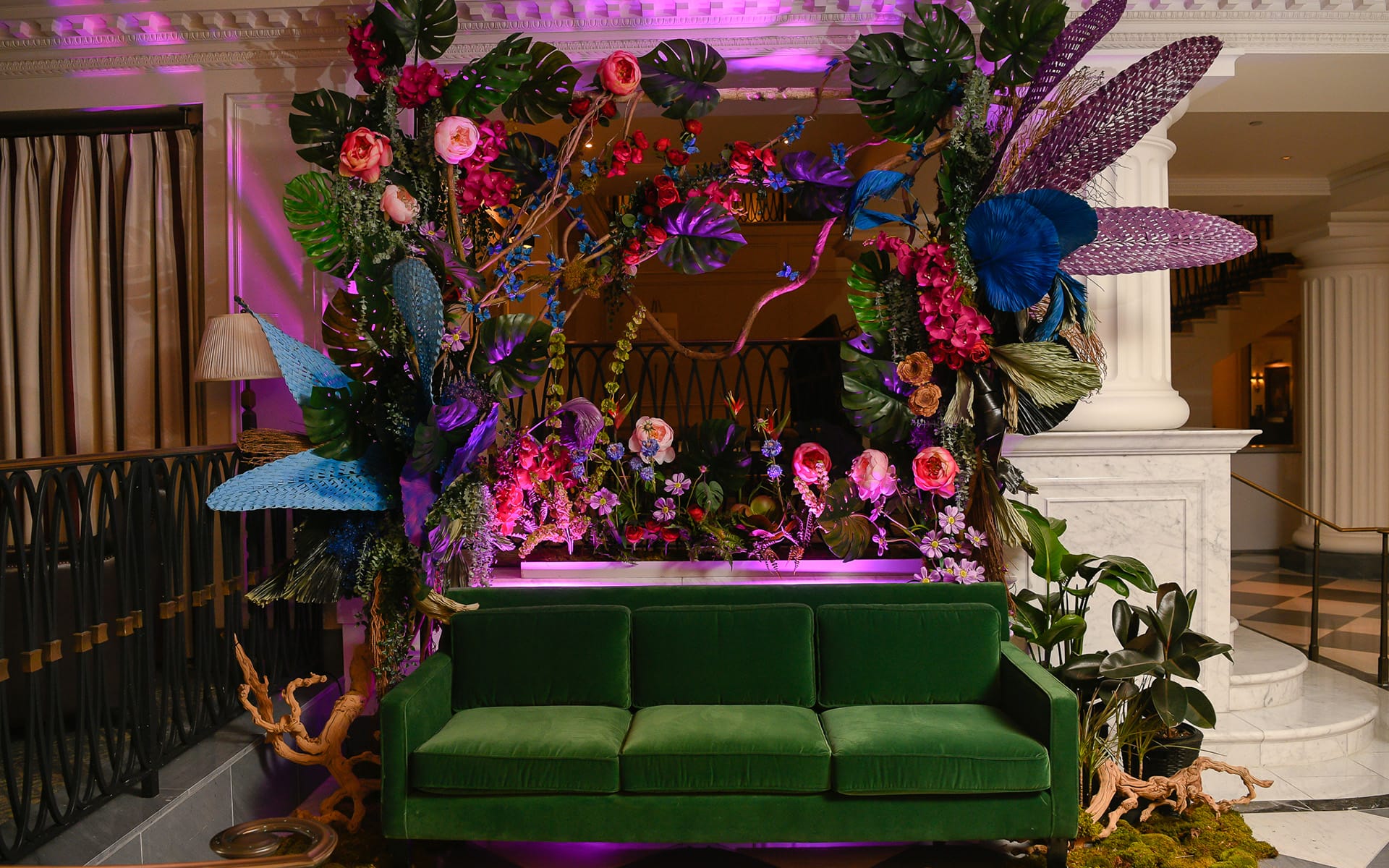 Vibrant floral and feather arrangement with a green sofa in an elegantly lit room with columns and checkered floor.