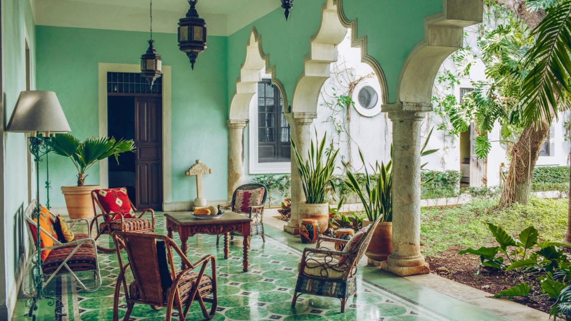Tropical veranda with green tiles, wicker chairs, plants, and decorative arches in an elegant and relaxing setting.