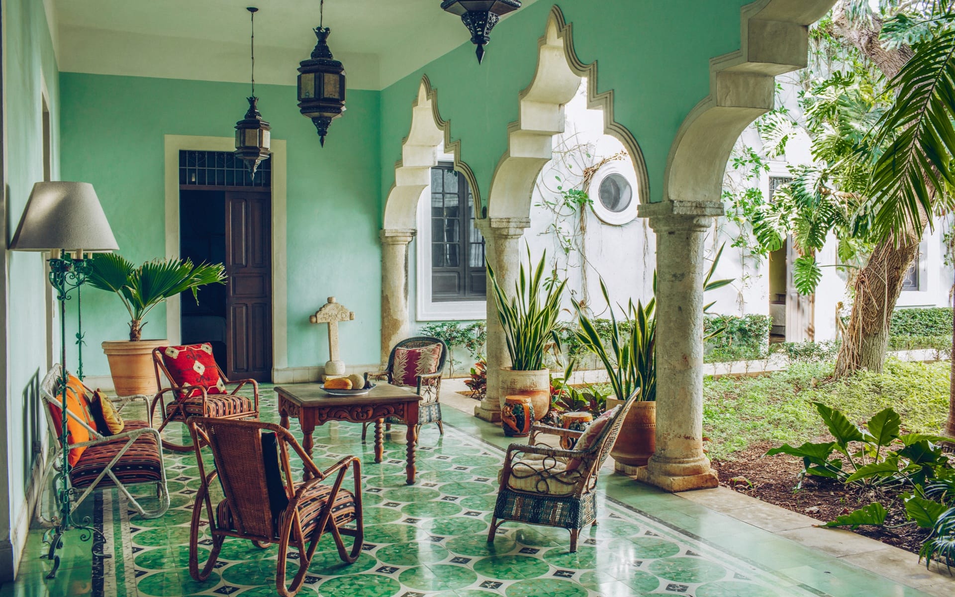 Tropical veranda with green tiles, wicker chairs, plants, and decorative arches in an elegant and relaxing setting.