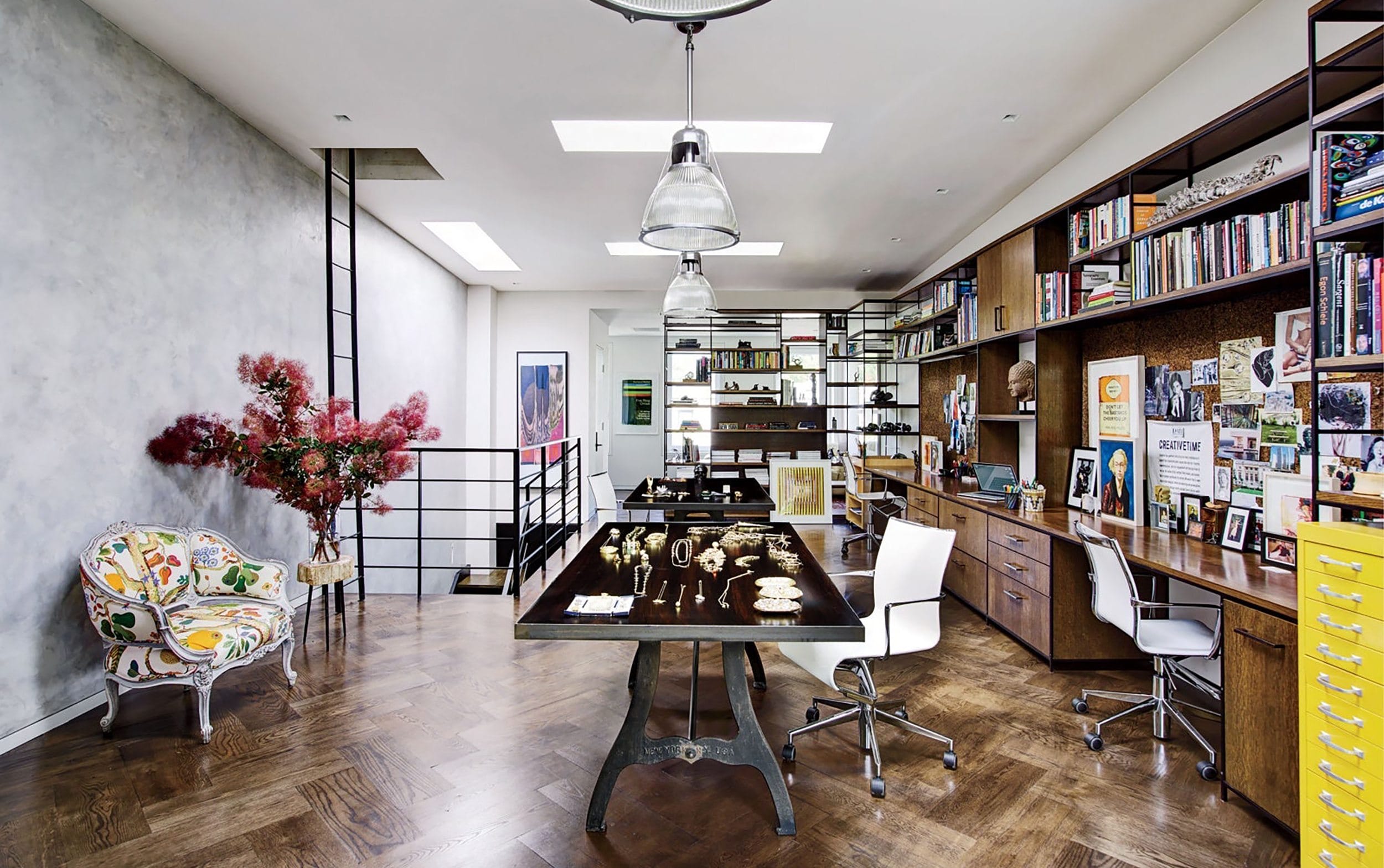 Modern home office with wooden floors, bookshelves, large desk, decorative chair, and ambient lighting.