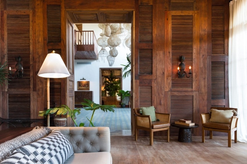 Cozy living room with wooden walls, seating area, hanging lamps, and view into another room with a large decorative chandelier