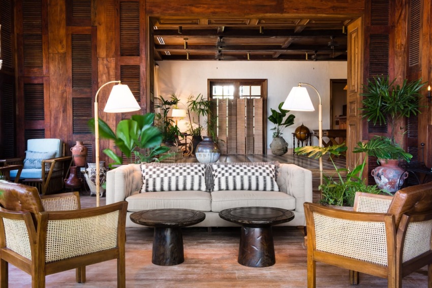 Cozy living room with a beige sofa, wooden chairs, indoor plants, and warm lighting.