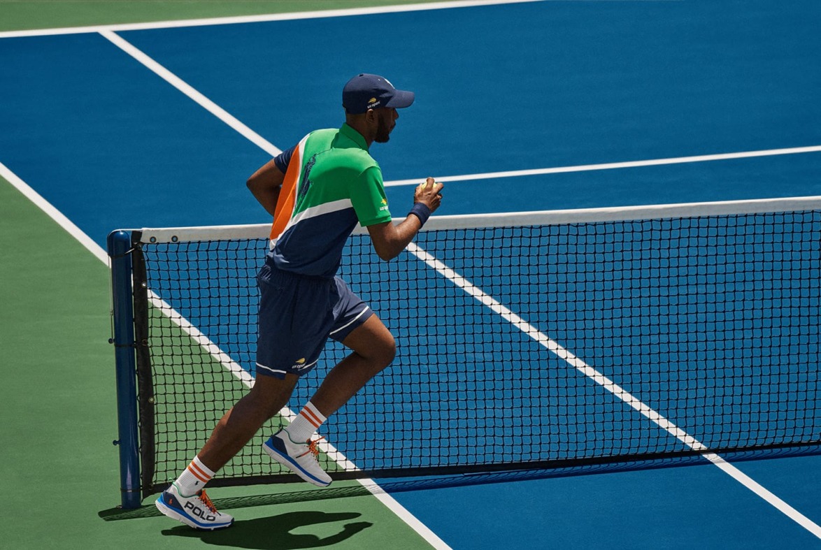Tennis player jogging on a blue and green court near the net during a match.
