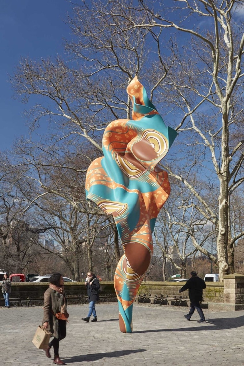 Colorful abstract sculpture in a park with pedestrians walking nearby on a clear day.