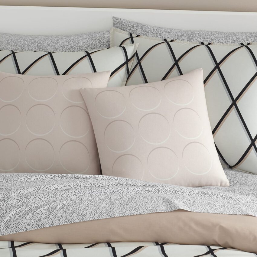 Beige and gray bedding with geometric patterns and two decorative pillows on a made bed.