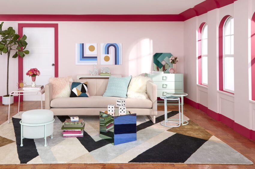 Modern living room with a beige sofa, colorful geometric decor, and pink accents on walls and furniture.