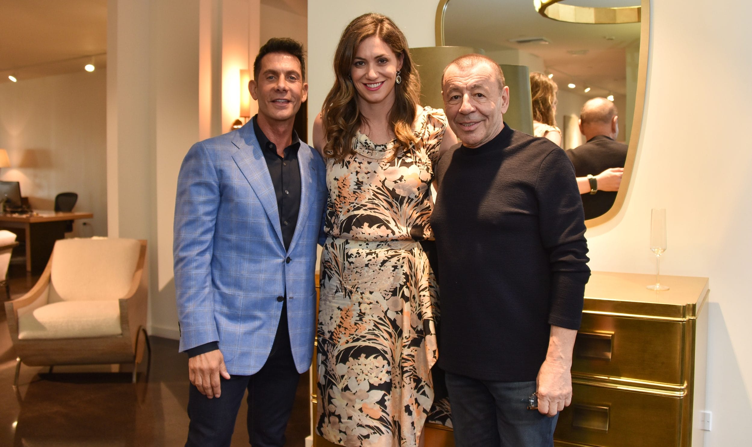 Three people smiling in a living room setting with modern decor and a gold cabinet in the background.