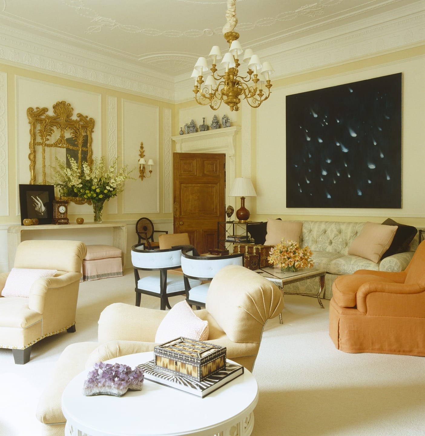 Elegant living room with plush chairs, large painting, and ornate chandelier, creating a sophisticated and warm atmosphere.