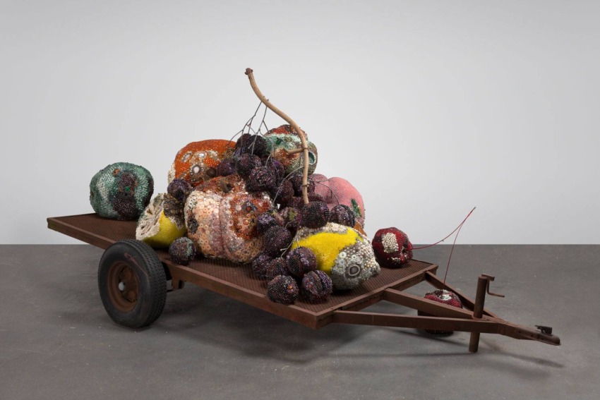 Colorful sculptural installation on a wooden cart featuring various spherical objects and textures against a plain background.