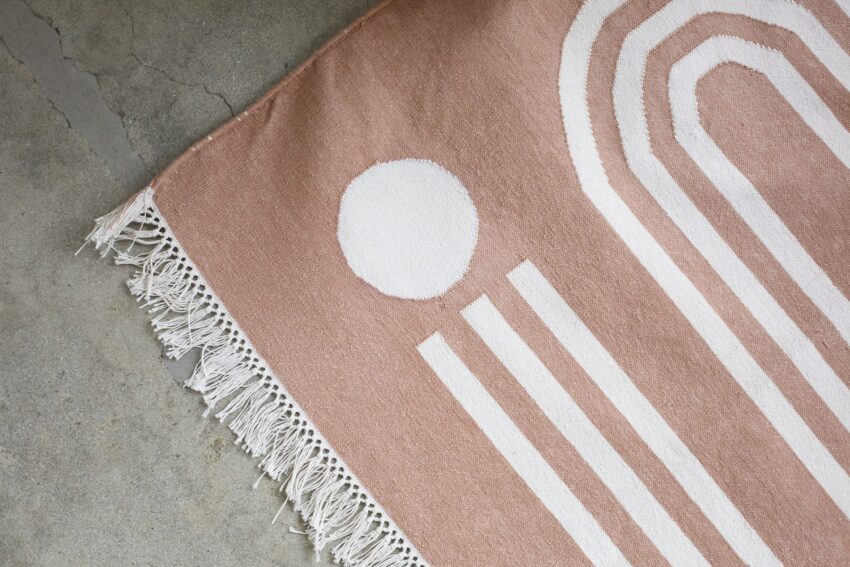 Woven rug with geometric white patterns and fringed edges on a concrete floor.